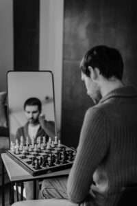 Homme assis face à un miroir et un échiquier, image du doute et du regard sur soi